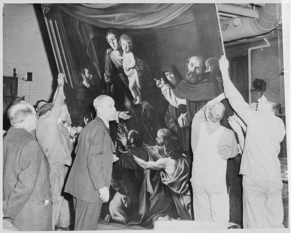 A black-and-white photo of workers in overalls and men in suits supporting Caravaggio's "Madonna of the Rosary" (Kunsthistorisches Museum, Vienna(