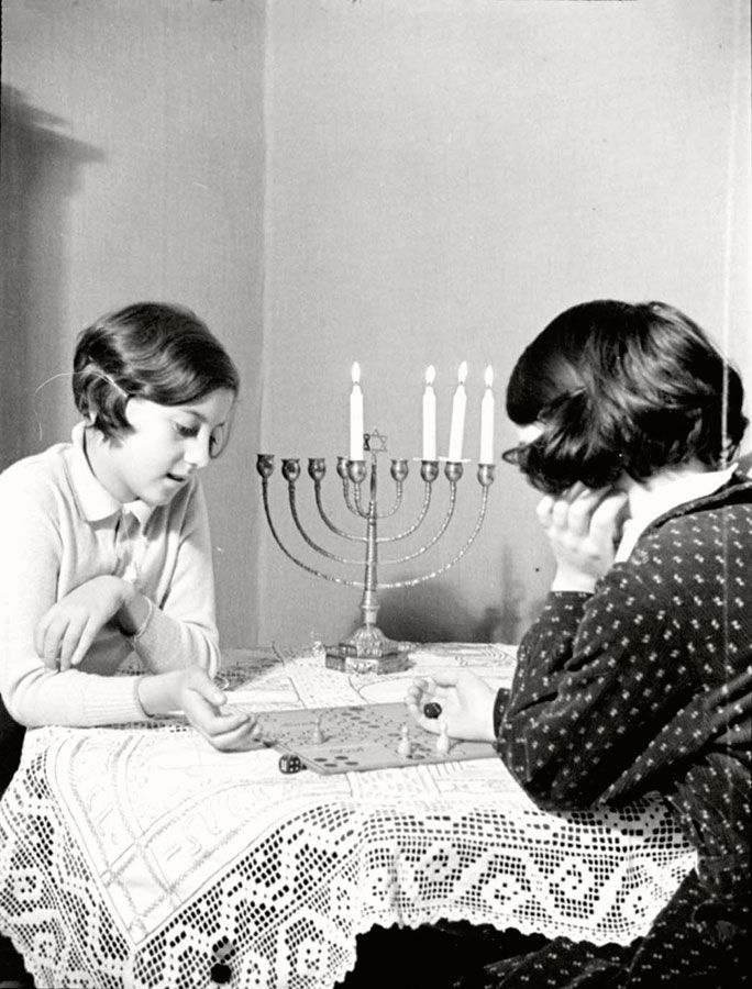 A black and white photo of two two girls playing the board game at a table with a Chanukiah (Menorah) with four candles burning