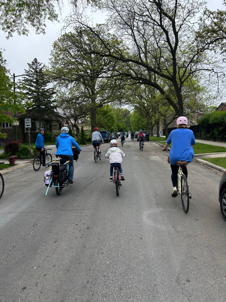 A group of parents and kids ride in a group down a residential street to school