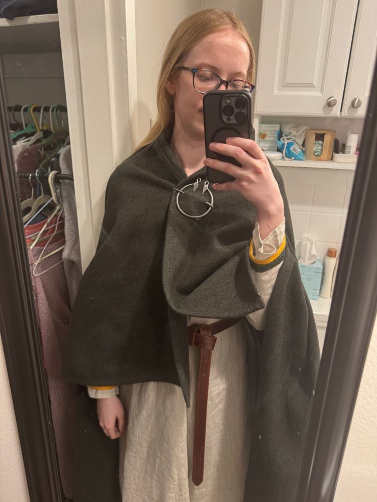 Me wearing a dark green cloak fastened with a metal brooch over a gray dress belted at the waist.