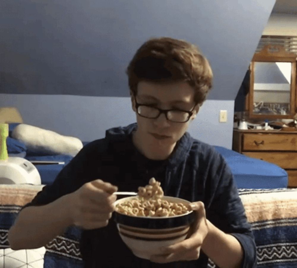 a young man with glasses is eating cereal from a bowl