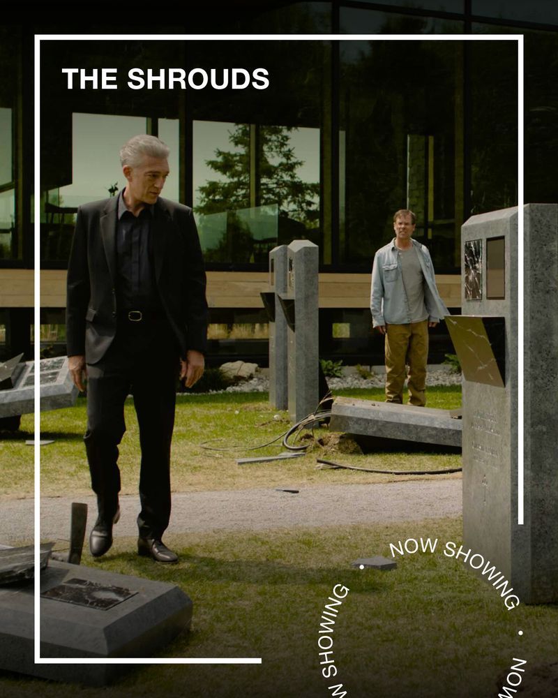 A man in a black suit stands in a futuristic graveyard. Text - The Shrouds, Now Showing.