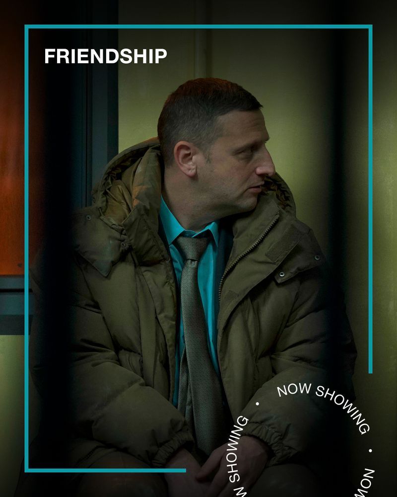 Two men, both wearing business clothes and jackets, look at each other with serious expressions. Text - Friendship, Now Showing.