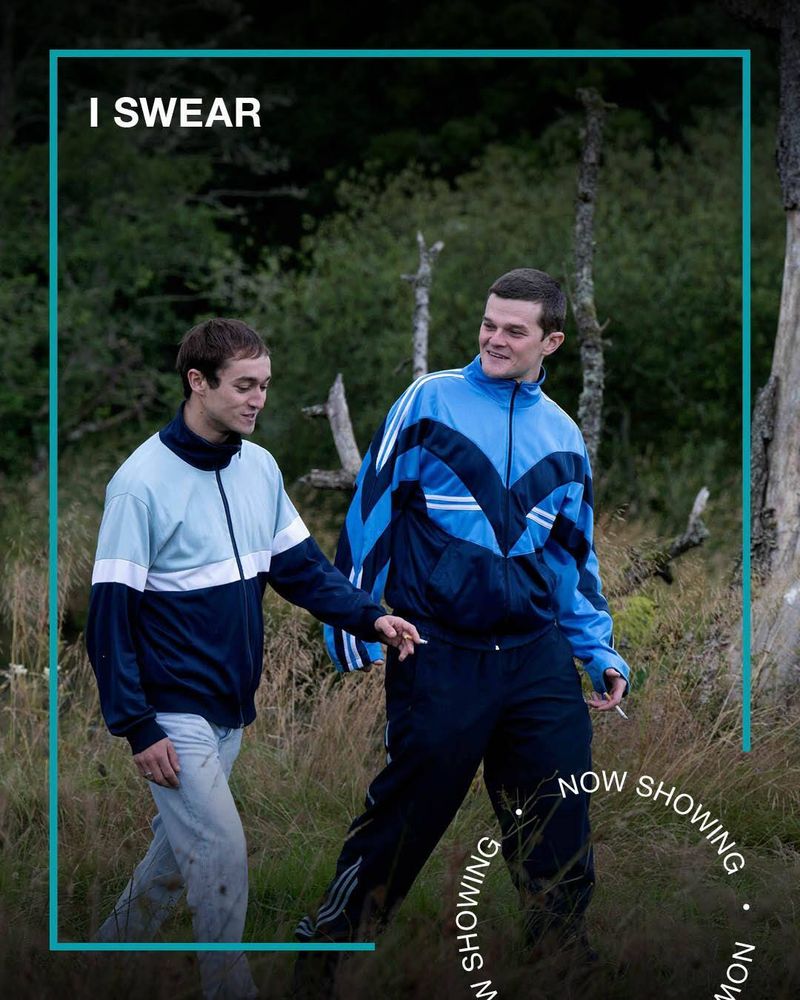 Two young men in shell suits walk through a forest talking. Text - I Swear, now Showing.