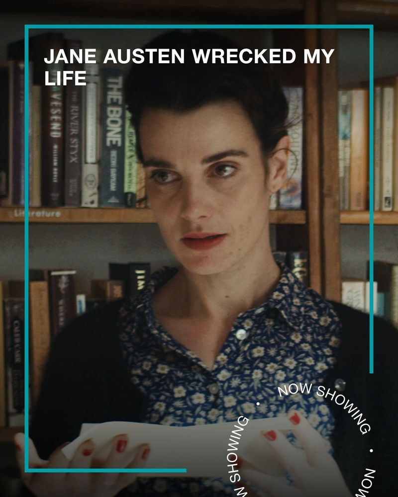 A woman stands in front of a book shelf, holding a note. Text - Jane Austen Wrecked My Life, Now Showing.