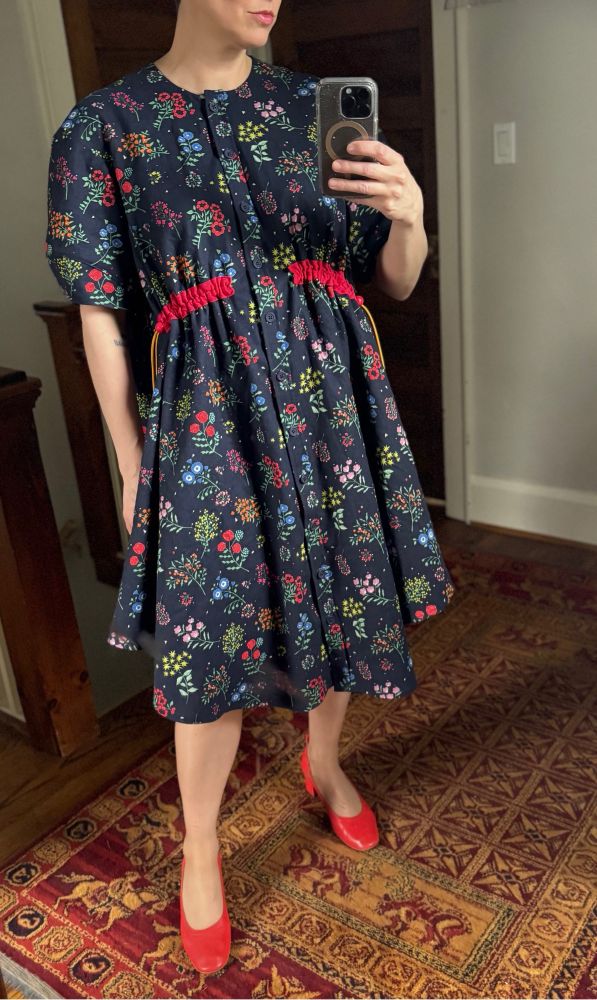 A person wearing a navy handmade dress with a tiny multicoloured floral pattern and red drawstrings at the waist.