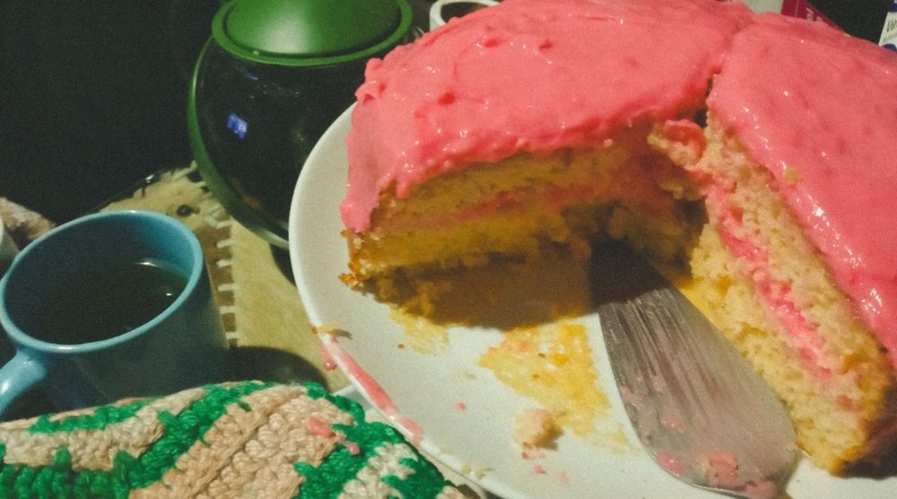 bolo de morango: massa com sabor de maracujá, recheio e cobertura de morango. bule verde de chá e caneca azul ao lado 