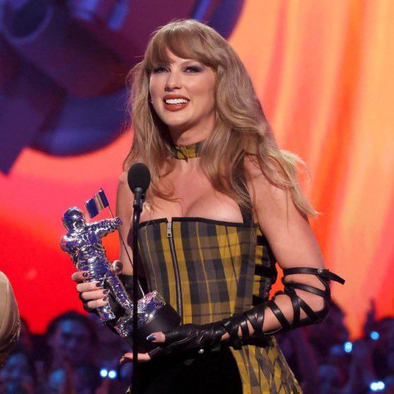 Taylor Swift receiving a VMA at the 2024 edition, wearing abplaid black and yellow dress