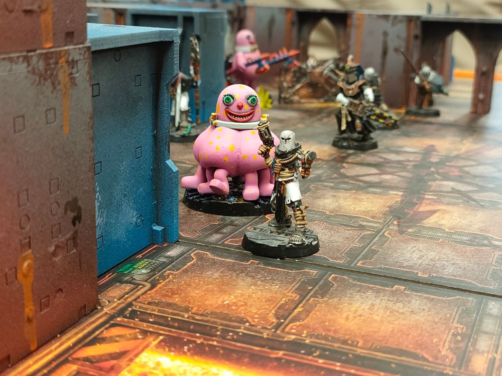 A Necromunda juve in front of a fire pit. Behind him, a horrifying mister bobby with a hundred legs sneaks up on him