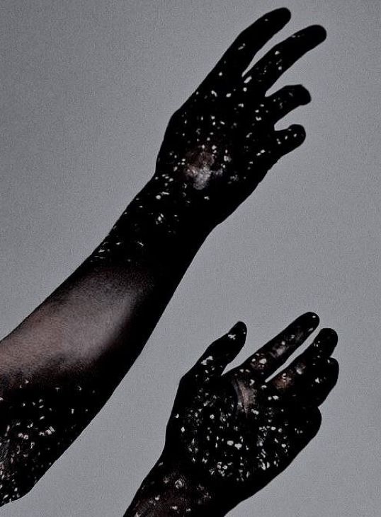 Photograph of a woman’s hands and forearms covered in black and white galaxy paint 