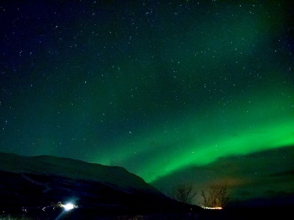 Photo of the aurora over Kiruna Sweden. The aurora is green, and the stars shine through it 