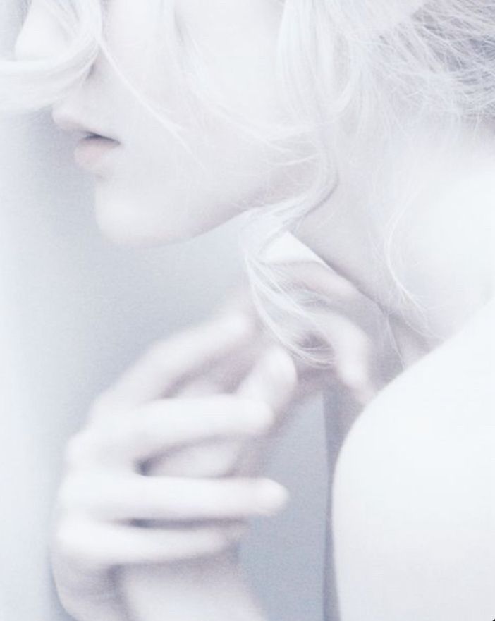 A photograph in shades of white and very pale gray of a woman. It’s zoomed in on her face and bare shoulders