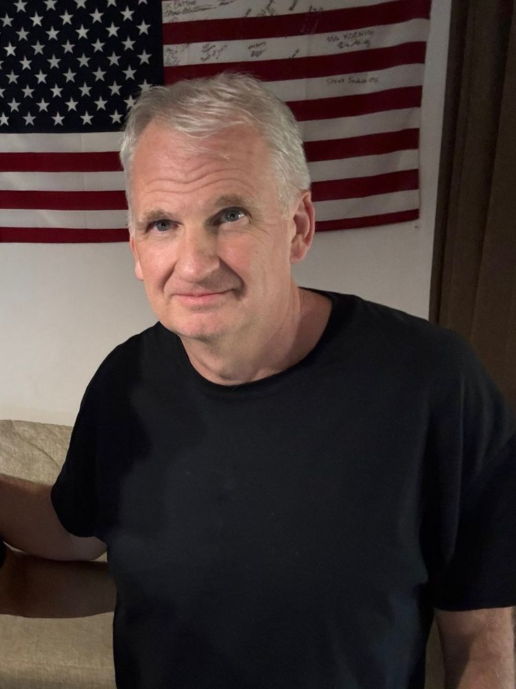 Timothy Snyder standing in front of an American flag hanging on a wall