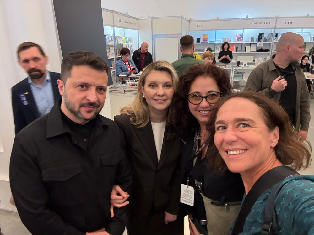 A selfie of Zelens’kyi, Zelens’ka, Shore, and Glaser standing together with a room of book displays behind them.