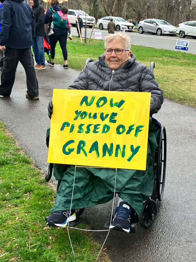 Woman sitting in a wheelchair holding a sign reading “now you’ve pissed off granny.”
