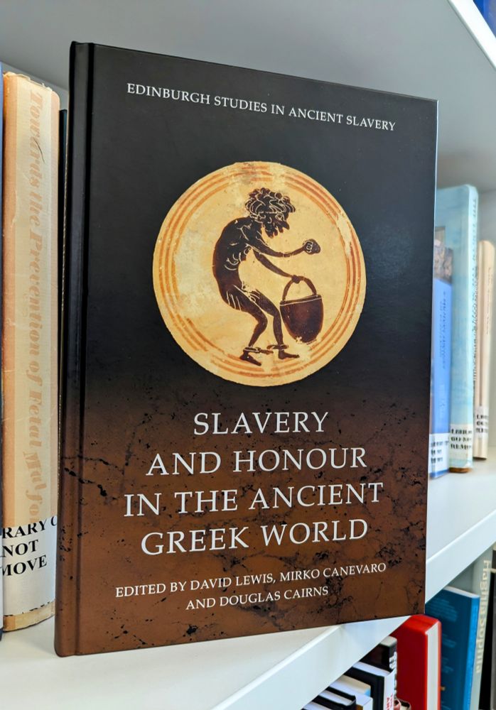 A photo of a hardback book, Slavery and Honour in the Ancient Greek World, edited by David Lewis, Mirko Canevaro and Douglas Cairns. The cover includes an ancient vase painting of a shackled humanoid figure.