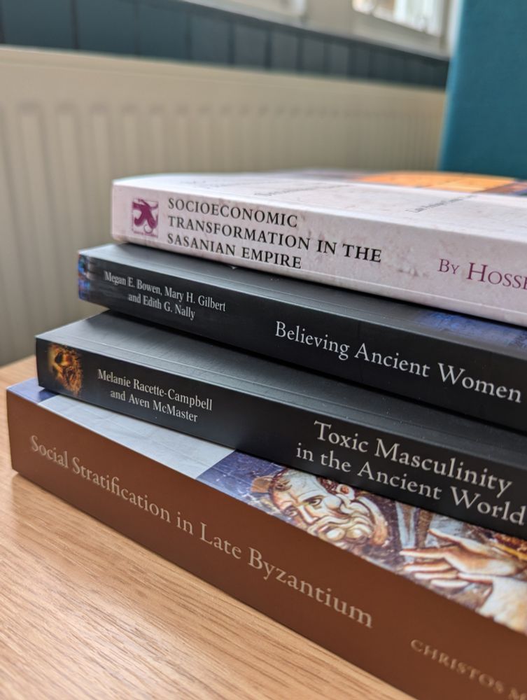 Photo of a stack of four books on a desk, their spines facing outwards so their titles can be read: Socioeconomic Transformation in the Sasanian Empire, Believing Ancient Women, Toxic Masculinity in the Ancient World and Social Stratification in Late Byzantium