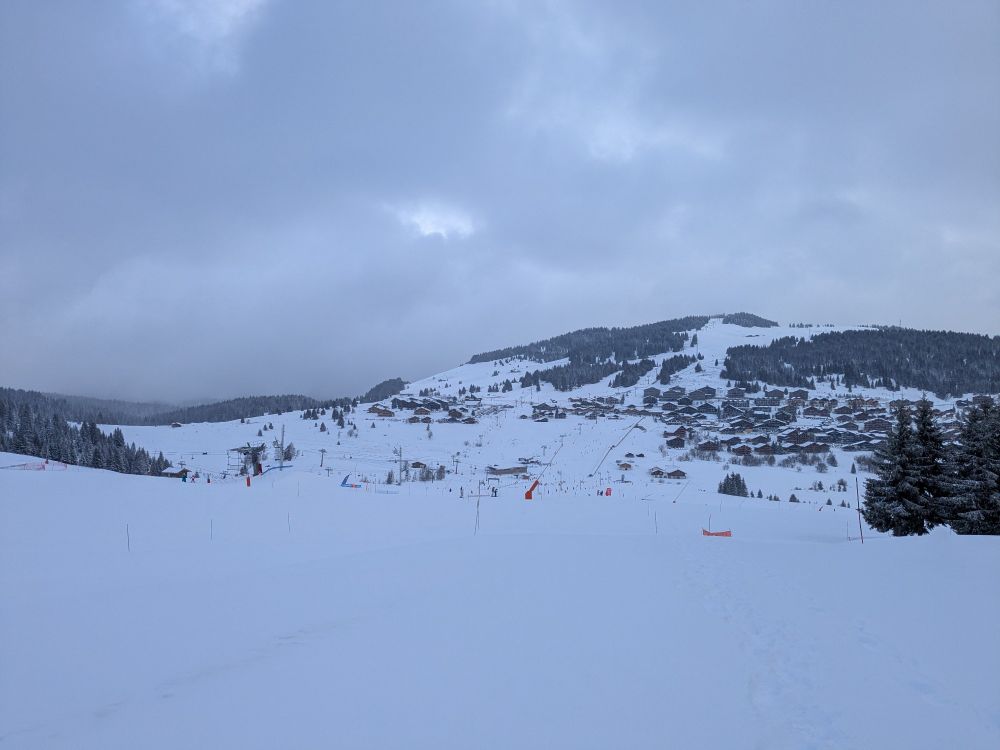 Paysage enneigé, on voit le village avec les sapins au-dessus et les télésièges 