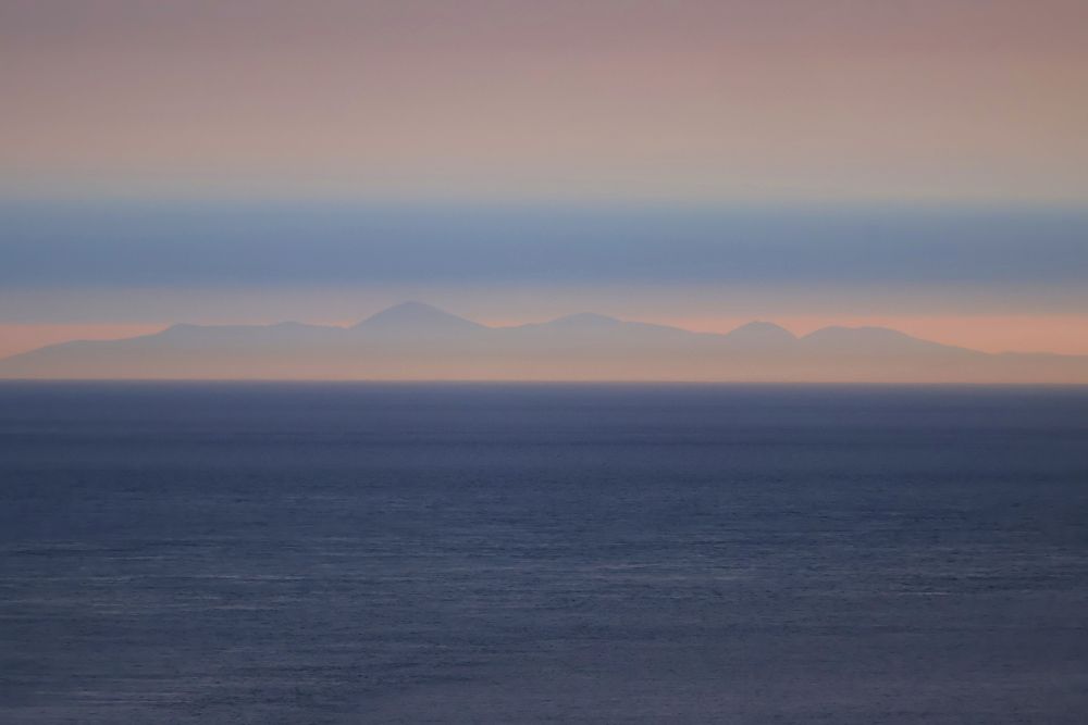 An evening view across the sea to Ireland from the Mull of Galloway lighthouse. The sky forms rose-coloured bands of mist above a band of blue, and the dark blue sea picks up hints of the pink sky.