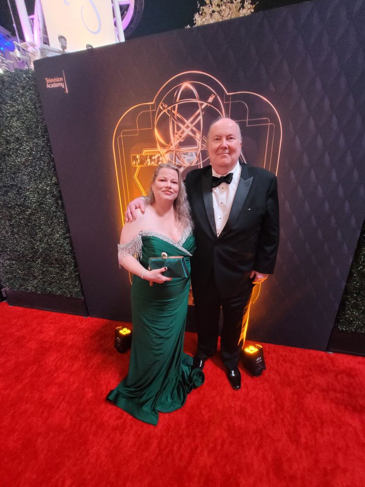 My husband and I at the 2024 Emmy awards. On the red carpet!!! Me dressed in an emerald green gown with silver beading in the front and sleeves are off the shoulder with sliver beading. My husband dressed in a black tuxedo.
