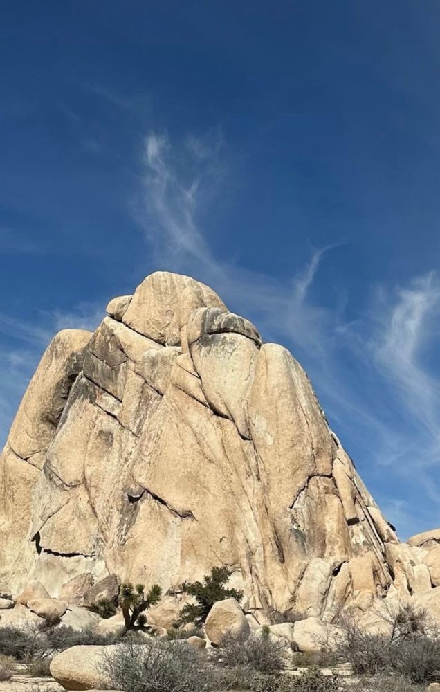 A large boulder formation with smaller boulders down below and a deep blue sky with some wispy white clouds above.