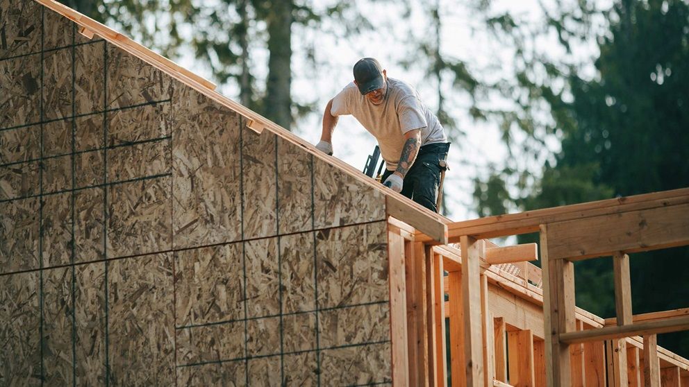 A photo of  a man working on the roof of an unfinished structure.