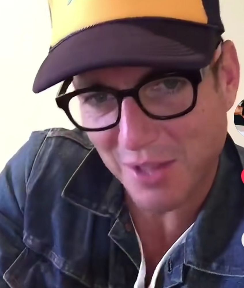 man in a trucker hat wearing glasses, purring his lips suggestively