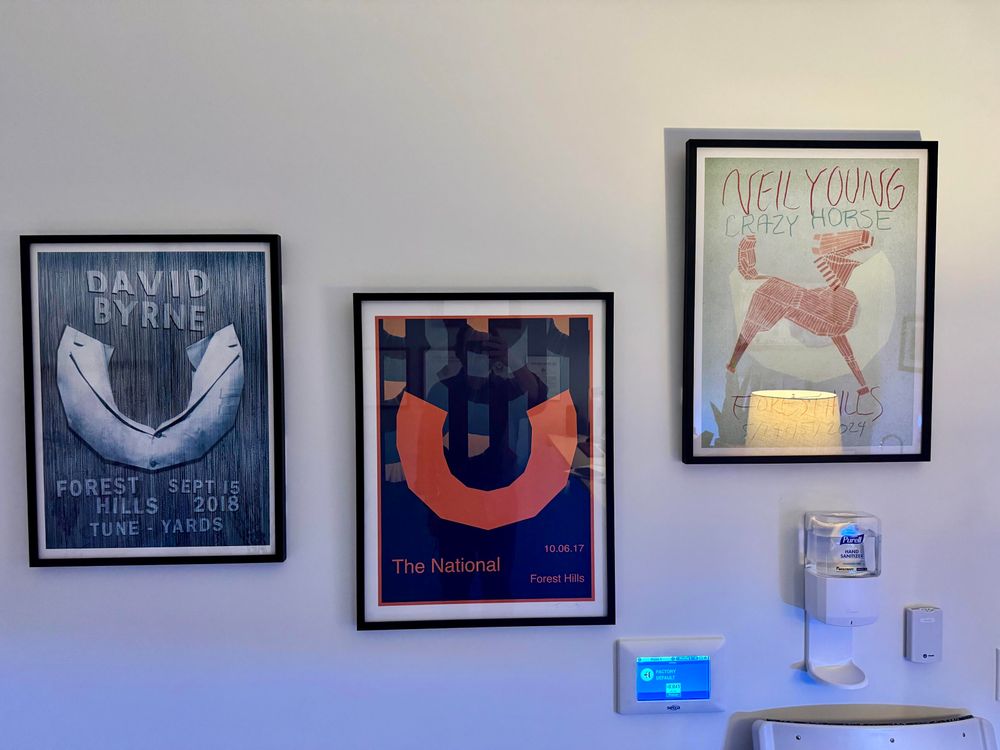 Forest hills posters: David Byrne, The National, Neil Young, framed and hanging on a wall above an lcd panel and a hand sanitizer dispenser