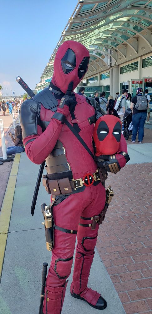 A person in Deadpool cosplay holding their finger to their lips while also holding a Deadpool head in their other hand.
