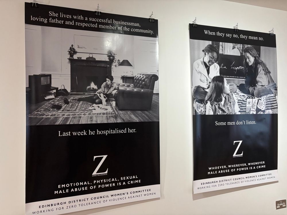 Photos of two black & white posters from the original Edinburgh Women’s Committee Zero Tolerance campaign. First poster shows a comfortable living room, a white woman sitting on the floor reading a magazine, accompanied by words: She lives with a successful businessman, loving father and respected member of the community. Last we he hospitalised her.” with the distinctive white Z on a black background of the Zero Tolerance campaign. The other poster shows a group of young women of mixed ethnicity in a relaxed group environment. Text reads: when they say no they mean no. Some men don’t listen.’ Again accompanied by the white Z.