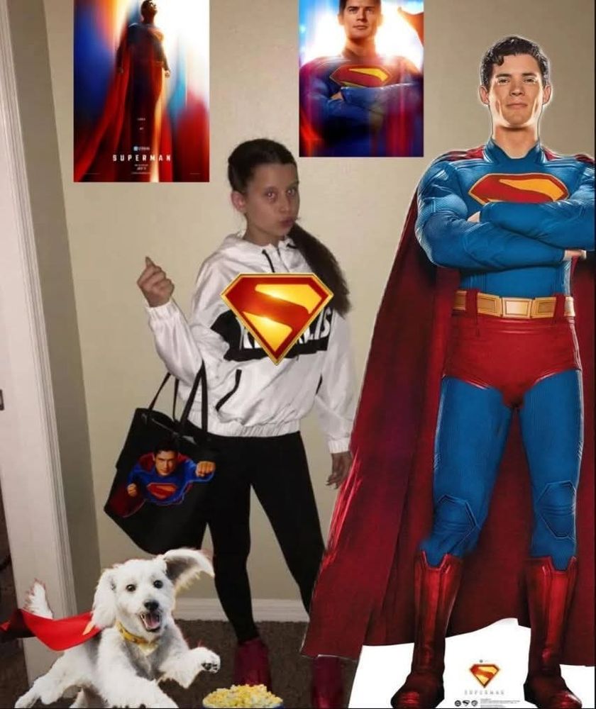 Meme of the girl who's the #1 fan, with Superman posters on the wall behind her, a life size Superman standee next to her, and Krypto the super dog in front of her as she poses wearing a Superman hoodie and Superman tote bag