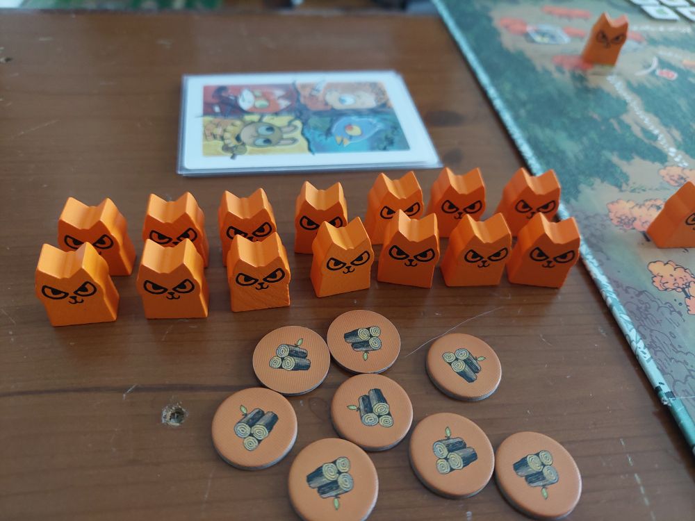 Photo of pieces from the board game Root, including 2 rows of 7 orange cat shaped wooden token, painted with wicked and mischievous scowls
