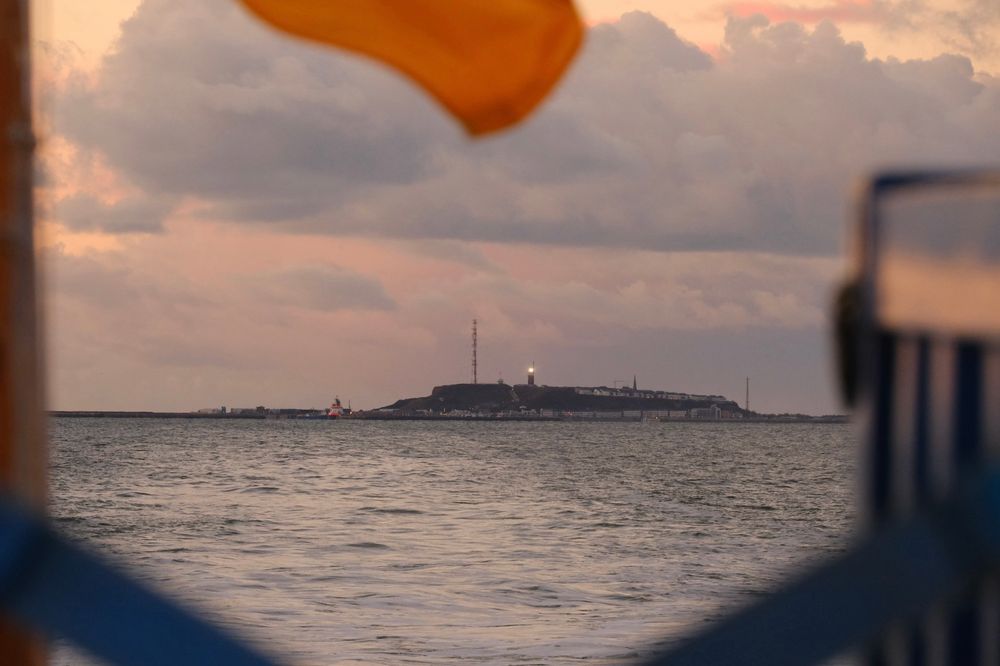 Eine Insel vom Schiff aus. Eingerahmt von zwei Containern und einem Teil einer Flagge in gelb