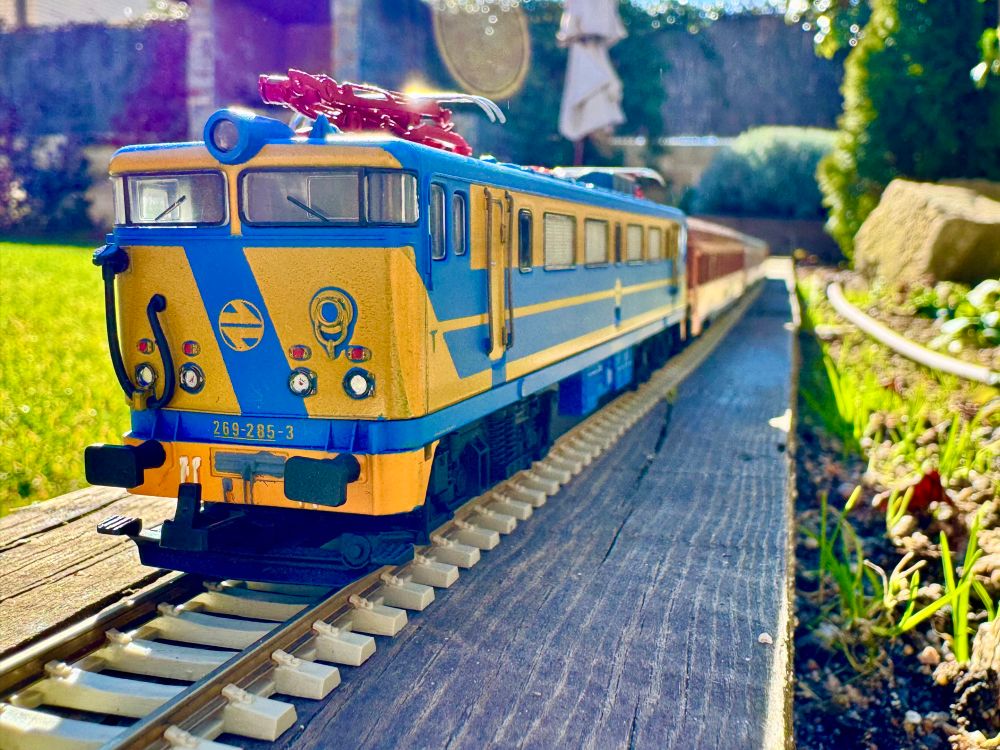 Tren a escala H0, fotografiado al aire libre. Locomotora 269 tirando de 5 coches (mix estrella y azul/amarillo)
