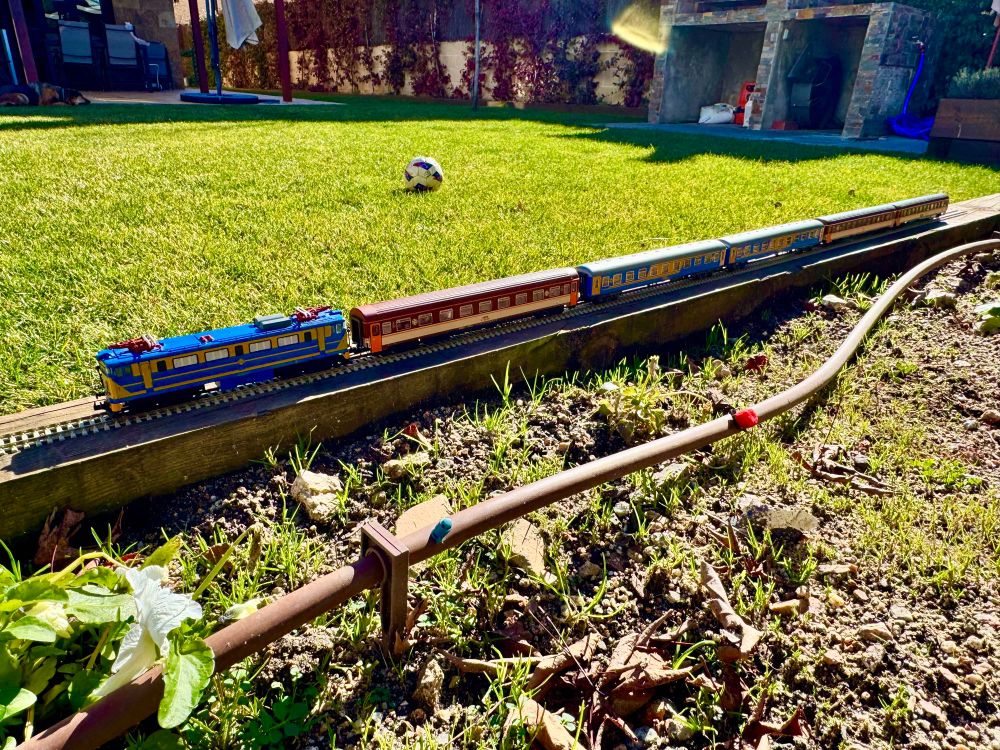 Tren a escala H0, fotografiado al aire libre. Locomotora 269 tirando de 5 coches (mix estrella y azul/amarillo). 