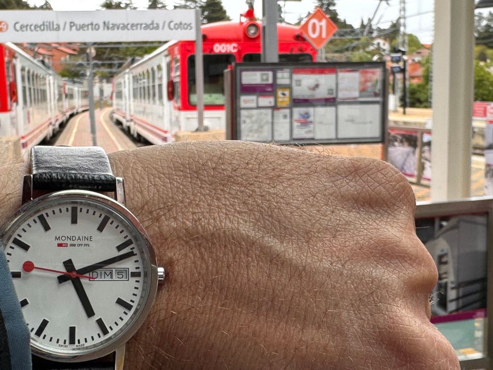 Reloj de pulsara, reproducción de los relojes de estación suizos, con los ya retirados trenes 442 de fondo, en Cercedilla, en el último día de circulación comercial de éstos