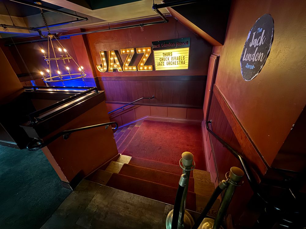 Stairway leading down to Jack London Review in Portland featuring a light up sign that says JAZZ and a marquis board with tonight’s performance by Chuck Israel’s Jazz Orchestra. 