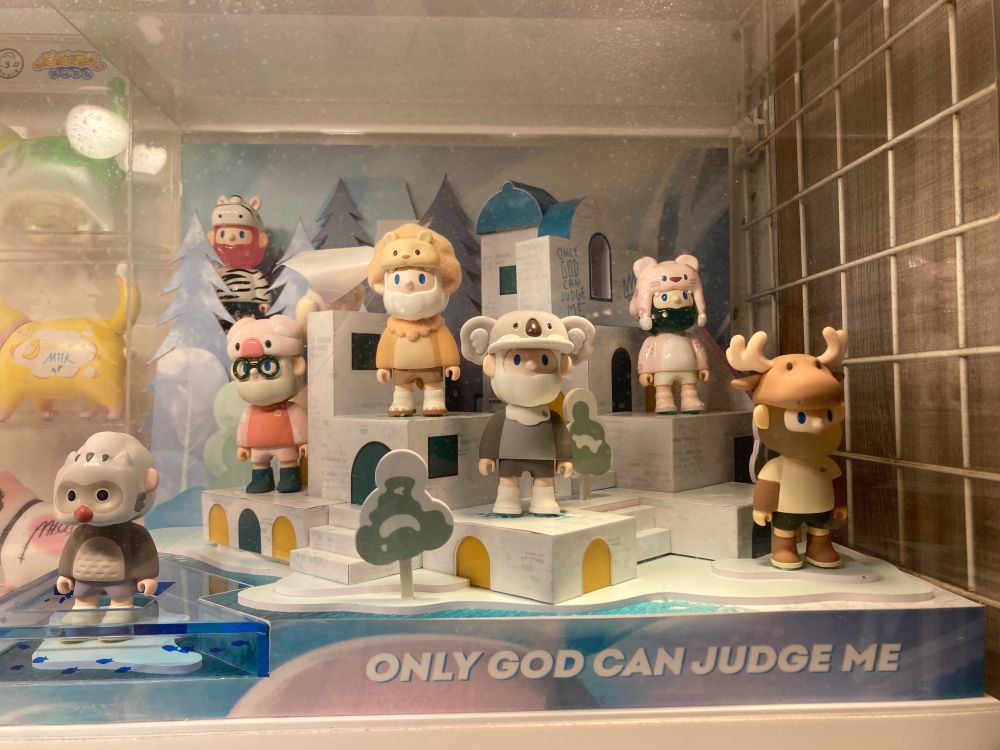 A set of random small toy figurines in a toy village, one has moose antlers, one has a koala hat, one is a monkey. Underneath them the caption reads "ONLY GOD CAN JUDGE ME."