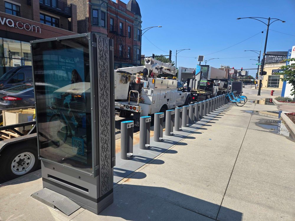 New electrified Divvy station being installed on the sidewalk at Halsted & Clybourn, with utility trucks and workers on-site.