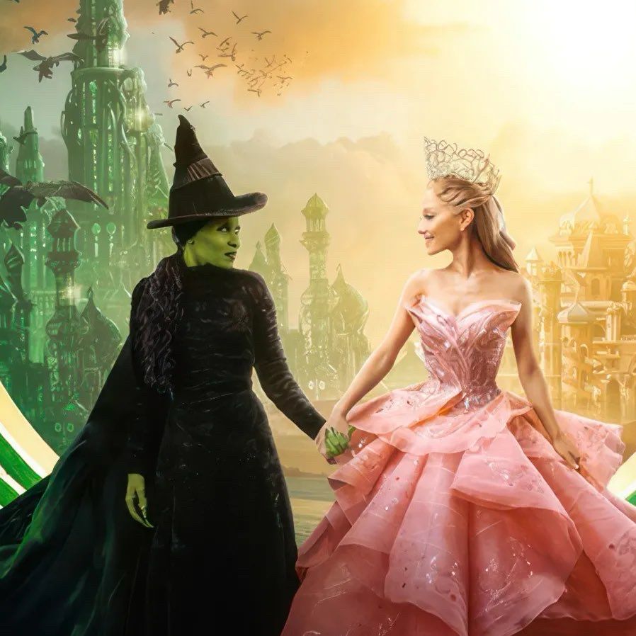Cynthia Erivo and Ariana Grande holding hands in ‘Wicked’ as they look at each other with Emerald City in the background. 