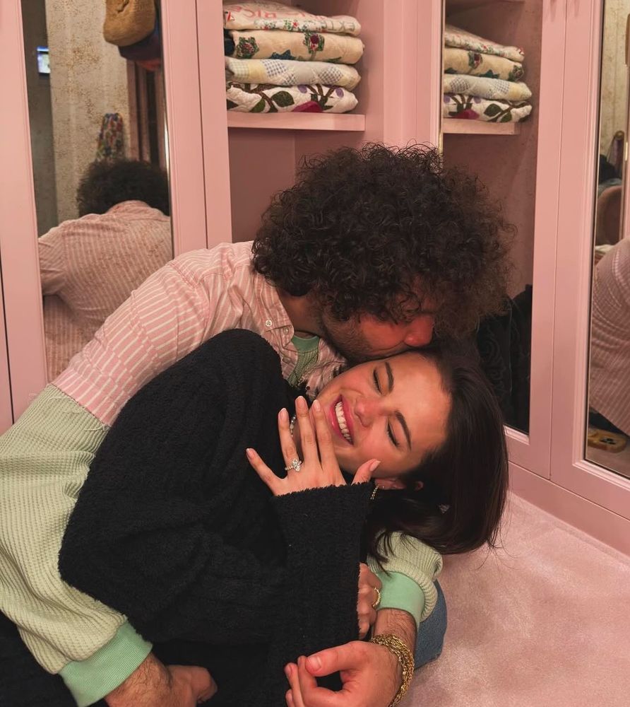 Photo of Selena Gomez and Benny Blanco hugging while she shows off ring. 