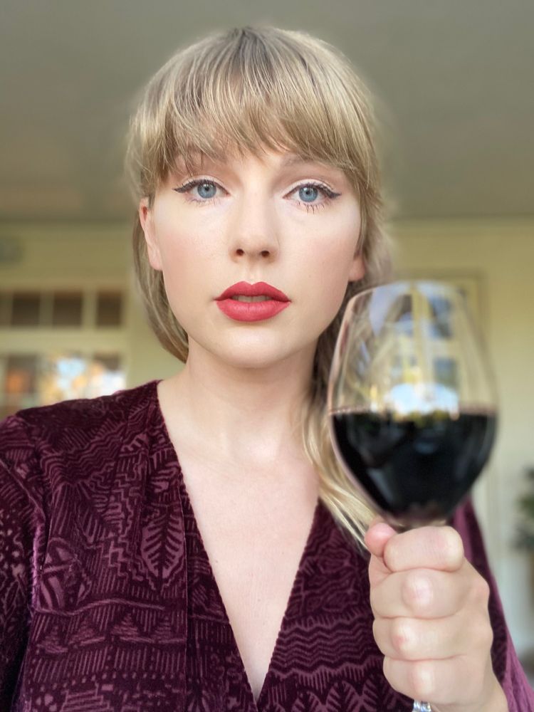 Photo of Taylor Swift aggressively gripping a glass of red wine. 