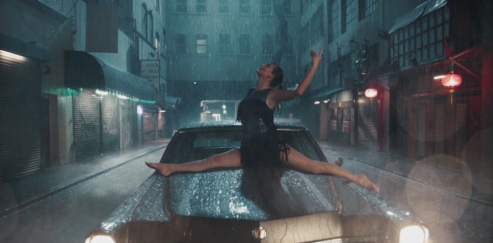 Taylor Swift doing the splits on top of the hood of a car as the rain falls on her in the ‘Delicate’ music video.