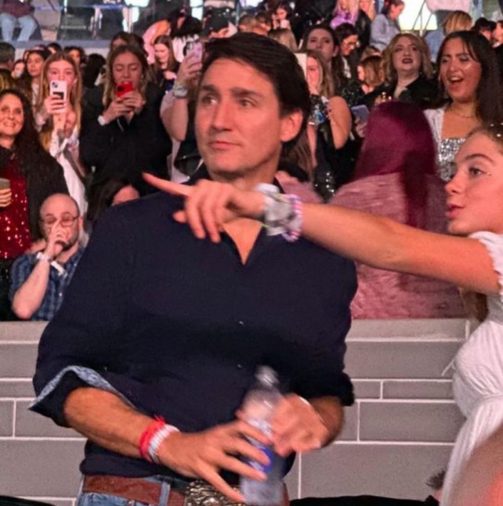 Photo of Justin Trudeau at Taylor Swift’s Eras Tour in Toronto holding water bottle while being given directions by a woman. 