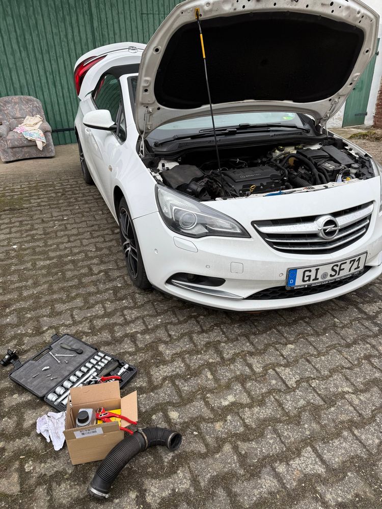 Ein weißer Opel Cascada mit offener Motorhaube, vorne Links im Bild ein Ratschenkasten und ein Ansaugstutzen