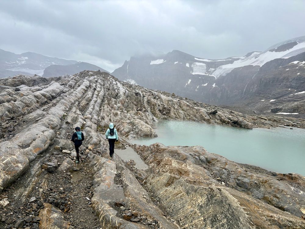 Two runners/hikers on rock groves formed by glaciers with an incoming storm and mountain peaks in the background