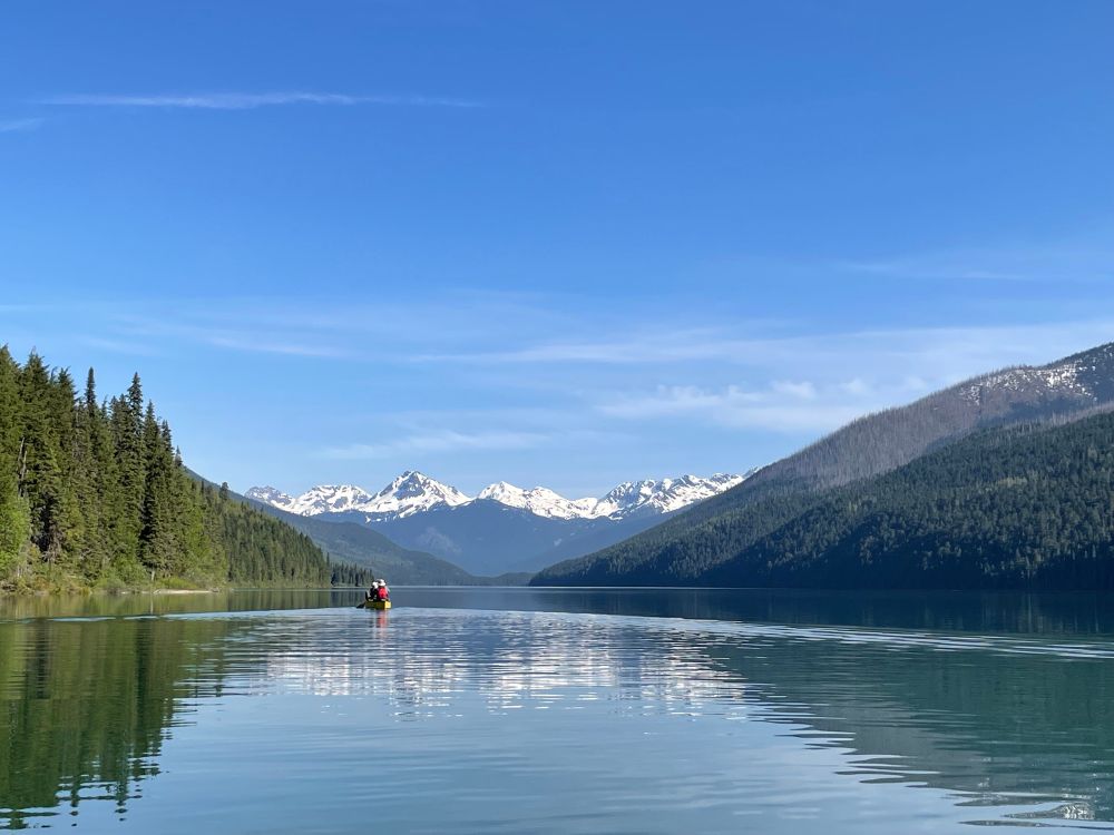 Canoe on lake headed towards white capped mountains 