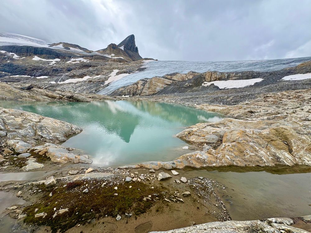 A glacier in the background dropping down to an aquamarine lake with a reflection of the mountains