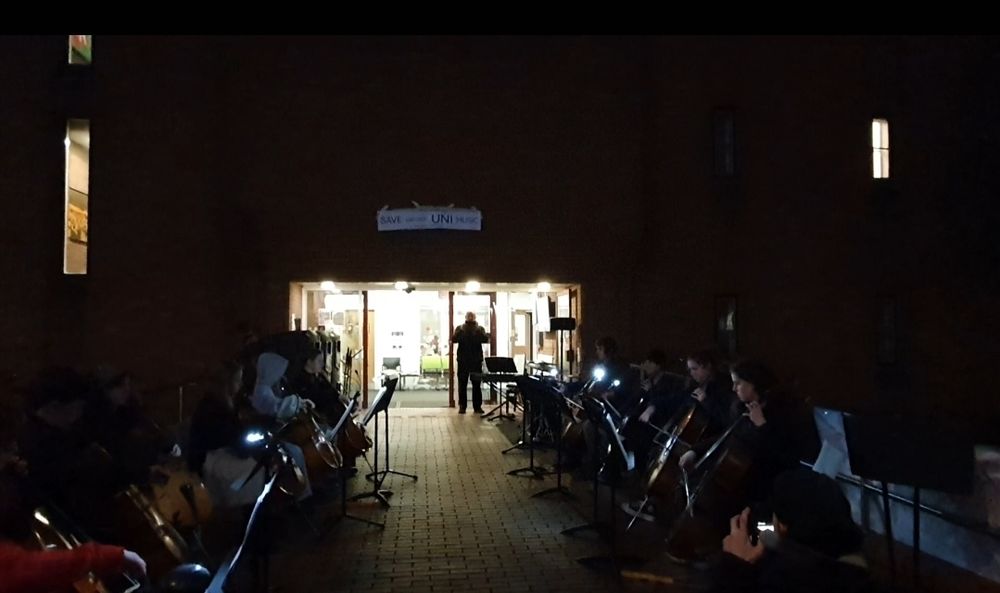In the dark, students play classical instruments outside a building doorway