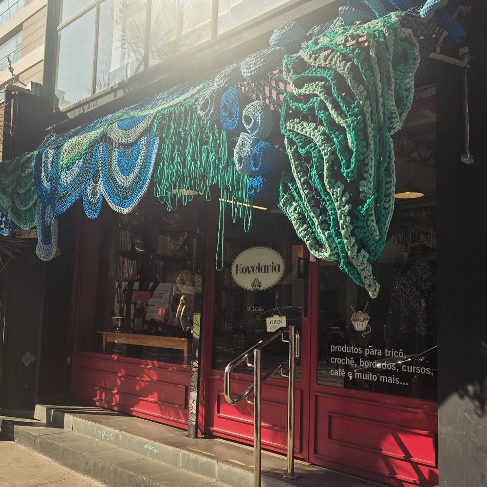 Fachada de uma loja chamada Novelaria enfeitada com um toldo de Crochê